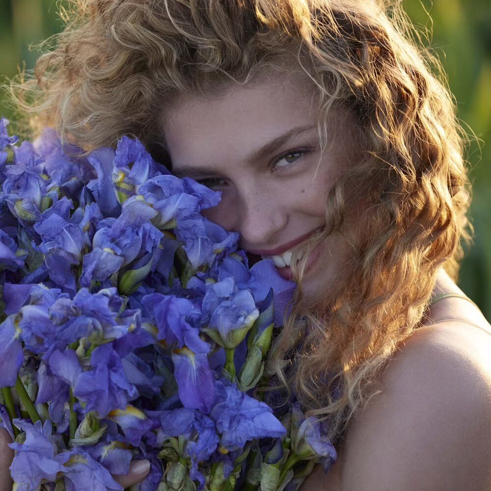 Porträt einer lächelnden Frau, die einen Strauß blauer Iris umarmt.