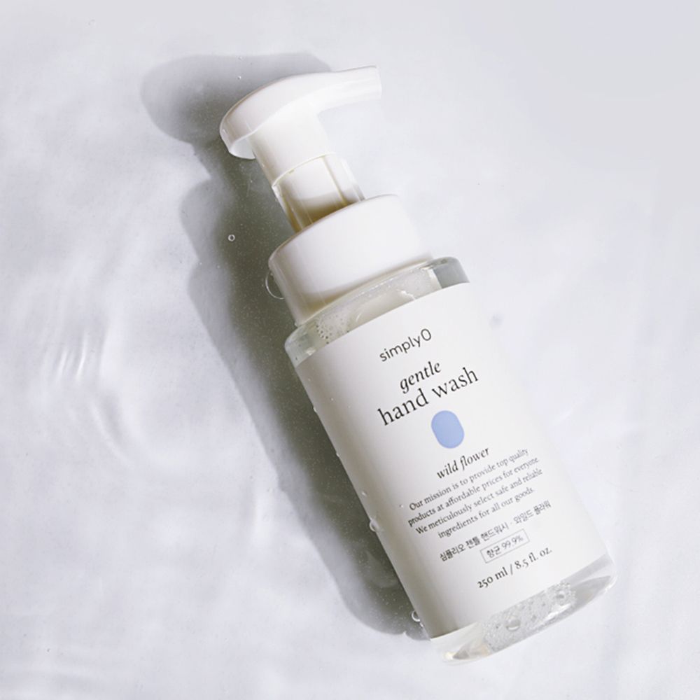 Transparente Flasche mit weißem Pumpkopf. Etikett mit Produktnamen und floralem Motiv. Auf Wasseroberfläche mit Schatten.