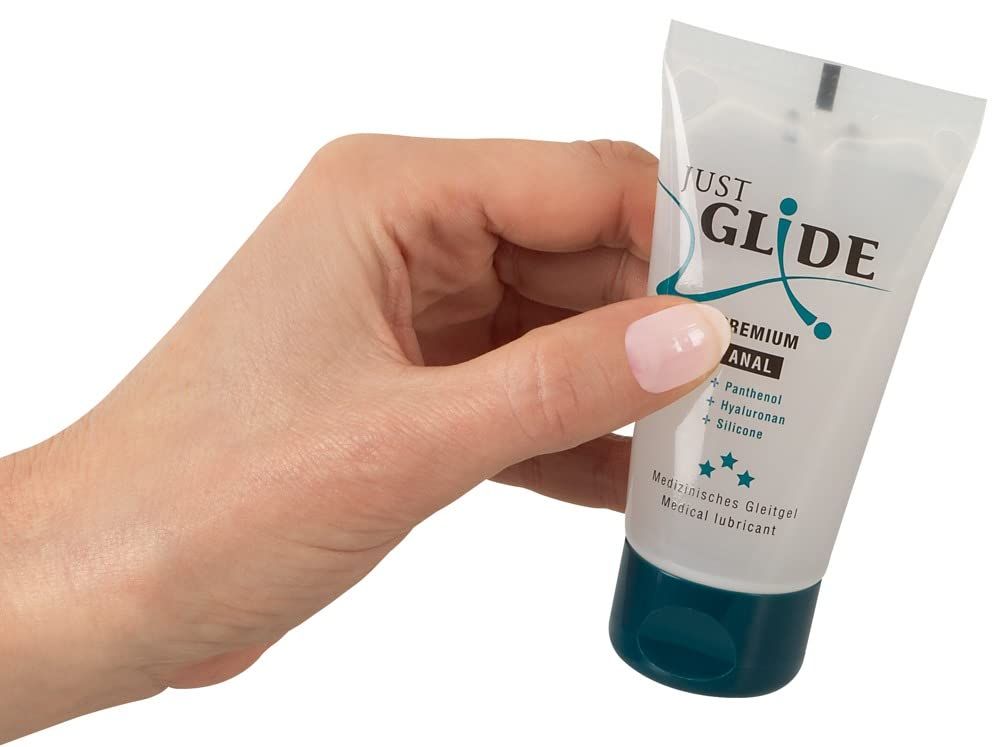 Hand hält Just Glide Premium Anal Gleitgel Tube. Transparenter Behälter mit blauem Verschluss.