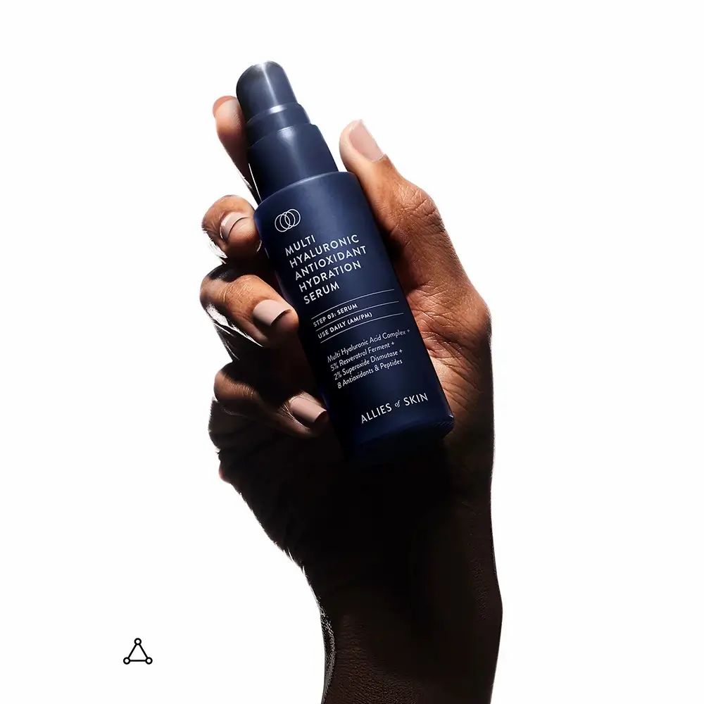 Hand hält dunkelblaue Flasche mit Pumpe. Aufschrift: Multi Hyaluronic Antioxidant Hydration Serum. Marke: ALLIES OF SKIN.