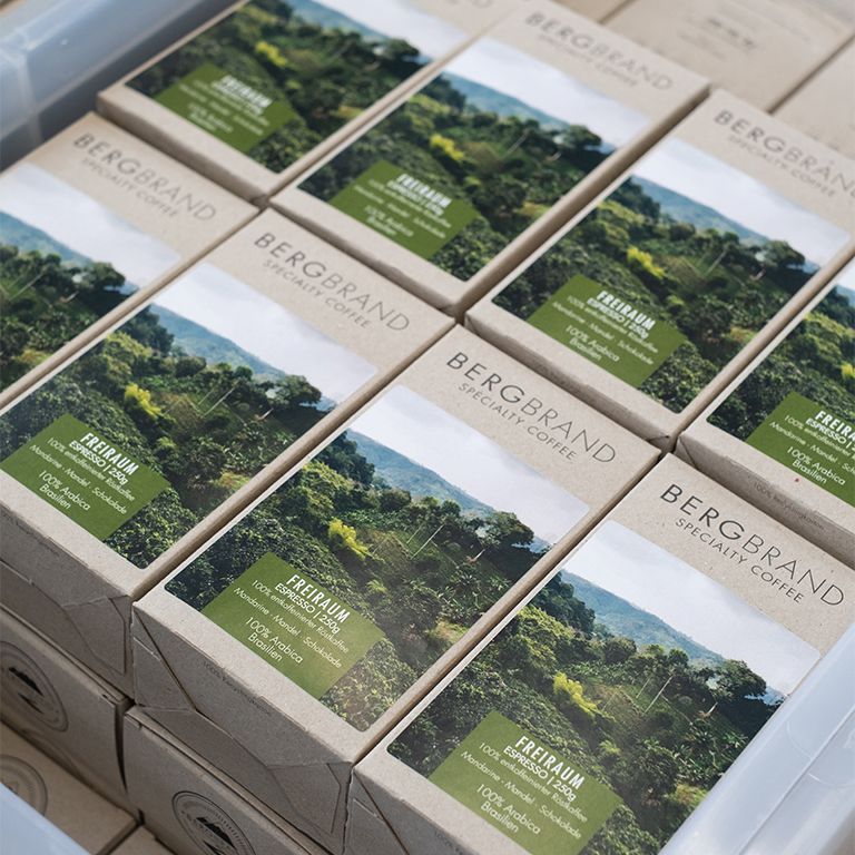 Mehrere Kaffeepackungen in einer Kiste. Text: BERGBRAND, Specialty Coffee, Freiraum Espresso, 100% Arabica, Brasilien.