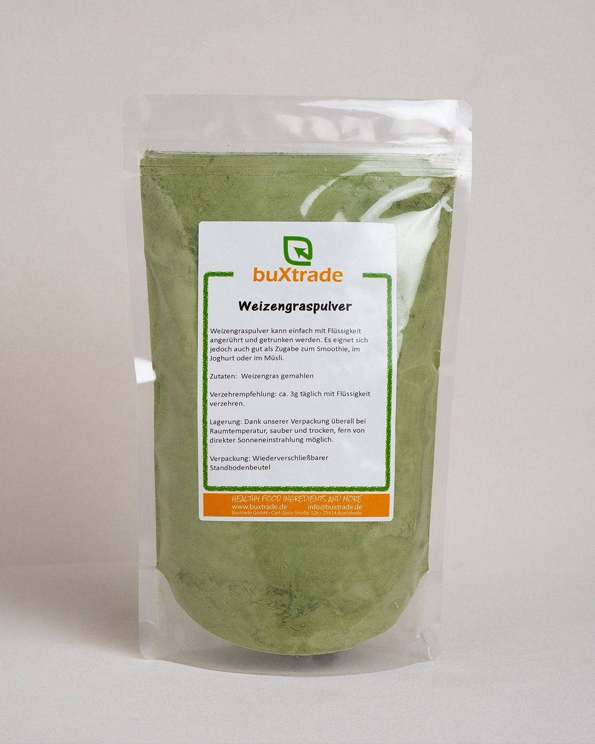 Transparente Verpackung mit grünem Pulver. Etikett mit Produktname 'buXtrade Weizengraspulver' und Text.