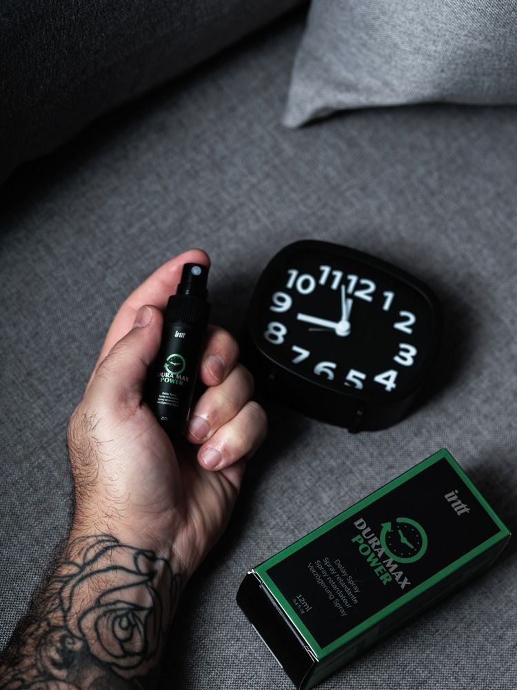 Hand hält eine schwarze Sprühflasche und eine Verpackung. Auf der Verpackung: "Dura Max Power" und Uhr-Symbol.