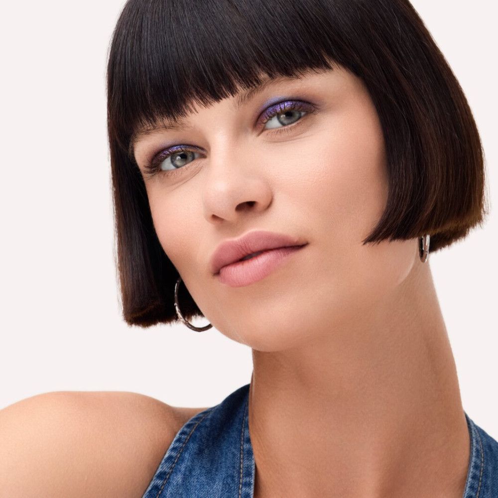 Porträt einer Frau mit dunklen Haaren und blauem Augen-Make-up. Sie trägt silberne Creolen. Ihr Blick ist direkt in die Kamera gerichtet.