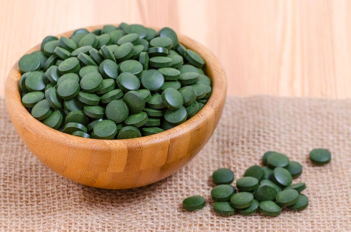 Hölzerne Schüssel mit grünen Chlorella-Tabletten. Einige Tabletten liegen daneben auf einem Leinentuch.