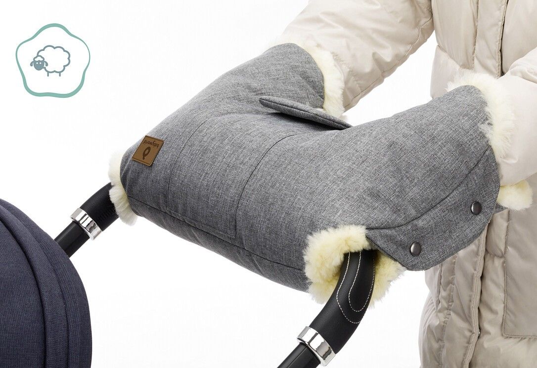 Handwärmer am Kinderwagen. Graues Außenmaterial, Lammfellbesatz. Logo-Etikett. Person trägt Jacke.