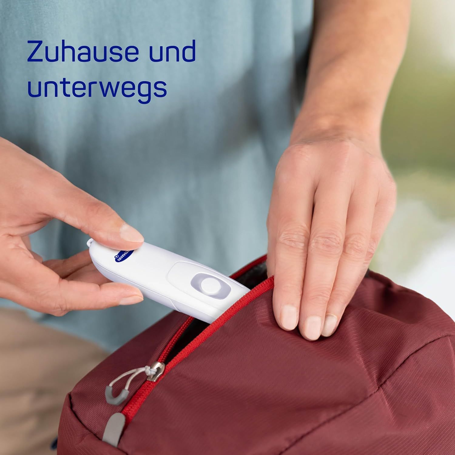 Person legt ein weißes, stiftförmiges Gerät in eine rote Tasche. Reißverschluss sichtbar.