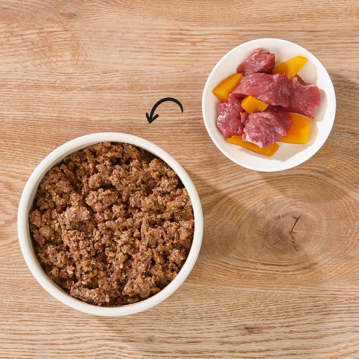 Zwei Schalen auf Holz. Eine Schale mit Hundefutter, eine mit Fleisch und Kürbisstücken.