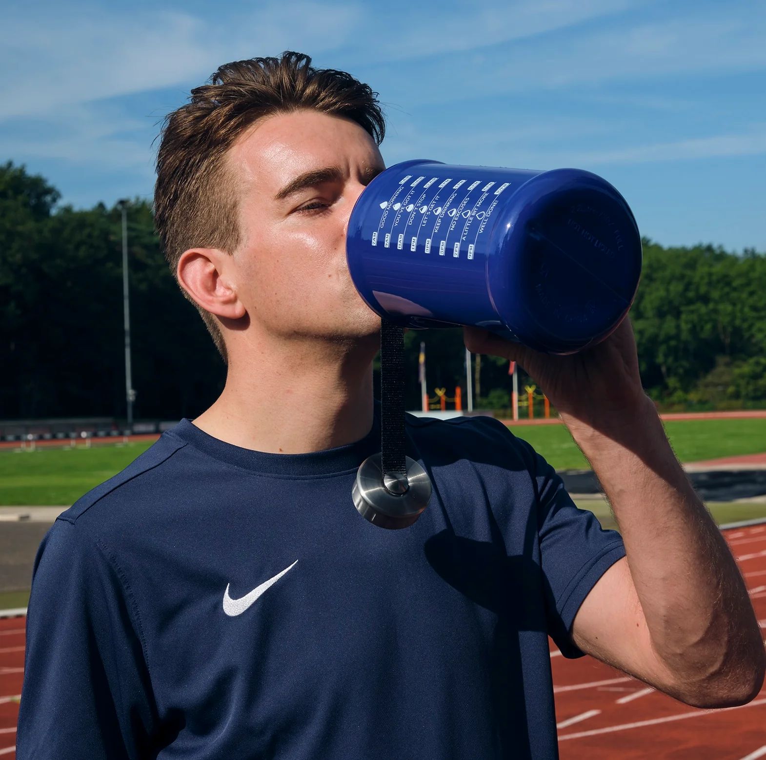 Person trinkt aus einer blauen Sportflasche. Die Flasche hat einen silbernen Deckel. Der Mann trägt ein blaues T-Shirt mit einem weißen Nike-Logo.