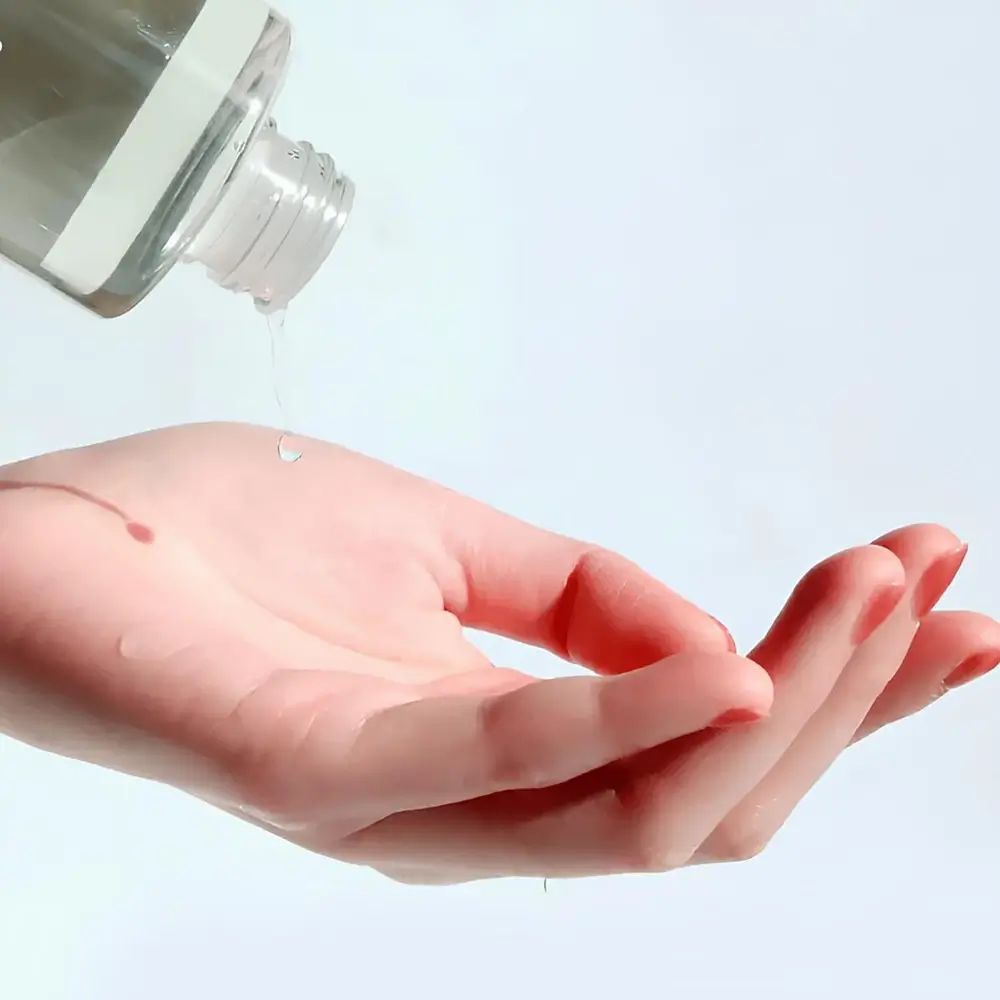 Klare Flüssigkeit tropft aus einer Flasche auf eine offene Handfläche.