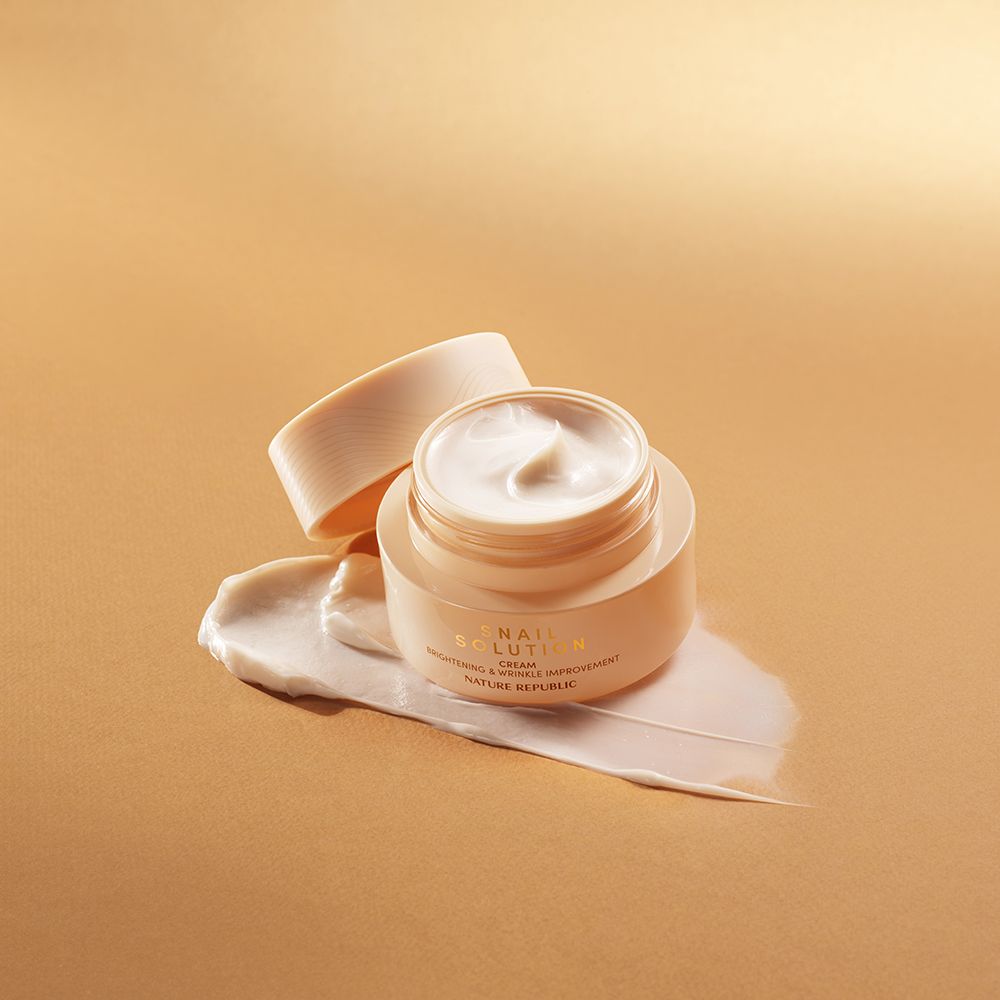Geöffnete Creme-Dose mit Creme-Klecks. Goldfarbene Schrift: Snail Solution Cream. Marke: NATURE REPUBLIC. Text: Brightening & Wrinkle Improvement.
