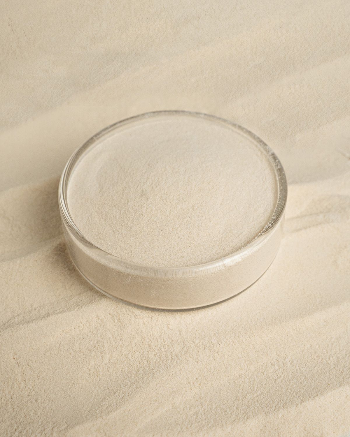 Nahaufnahme von Agar Agar Pulver in einer runden Schale auf sandigem Untergrund.
