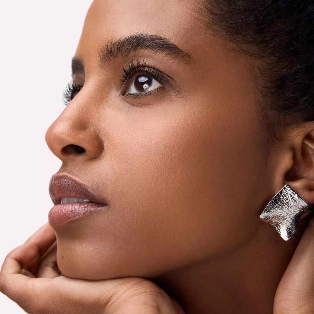 Porträt einer Frau mit langen Wimpern. Sie trägt Ohrringe.