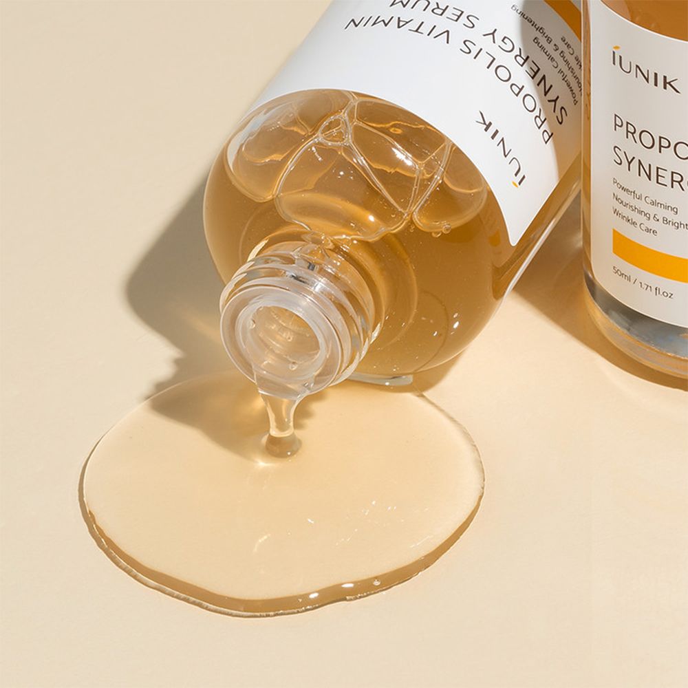 iUNIK Propolis Vitamin Synergy Serum fließt aus einer Flasche. Serum ist goldgelb.