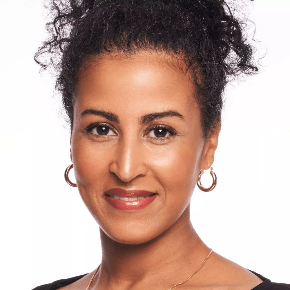 Porträt einer Frau mit dunkler Haut und Locken. Sie trägt goldene Ohrringe und ein schwarzes Oberteil.