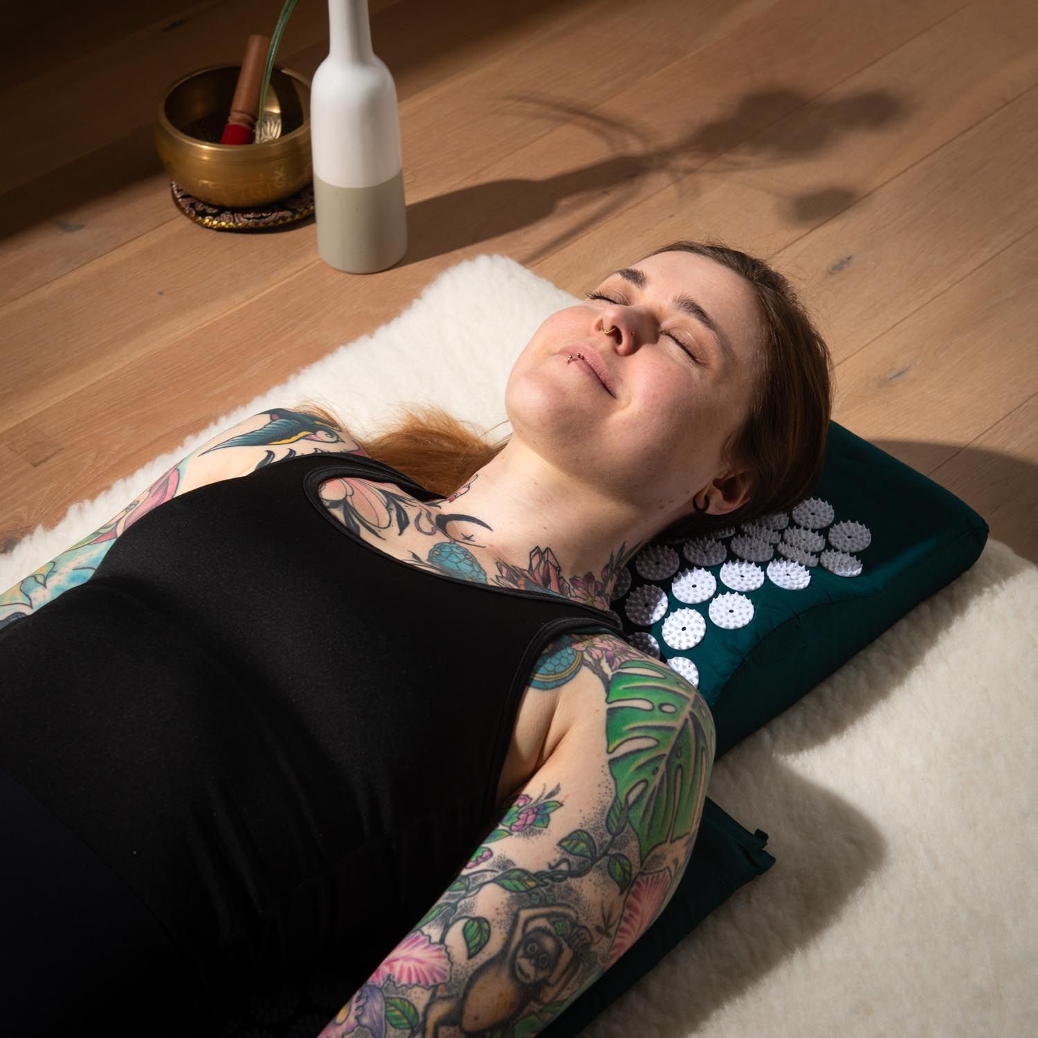 Person liegt auf Akupressur-Kissen. Dunkelgrünes Kissen mit weißen Noppen. Person mit Tattoos.