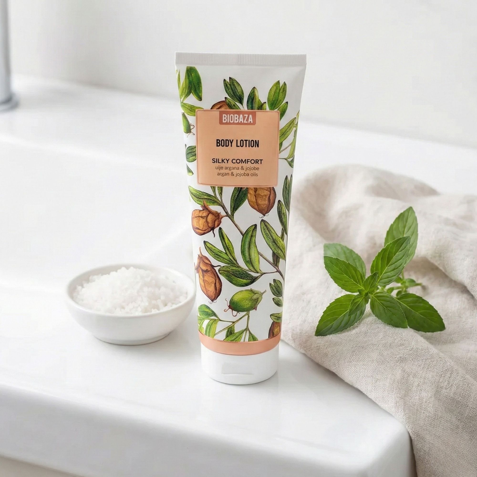 Körperlotion-Tube mit floralem Design. Daneben: Schale mit Salz, Blätter und ein Handtuch.