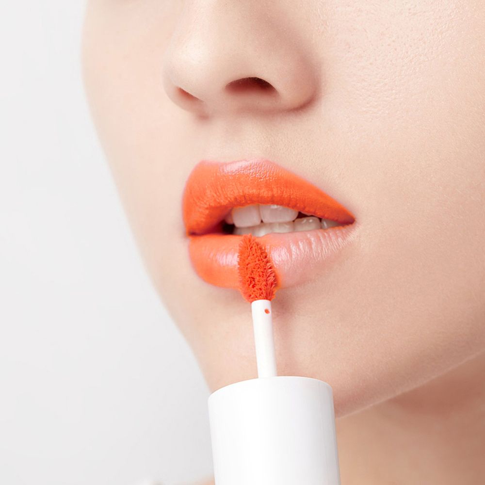 Nahaufnahme von Lippen, die mit einem orangefarbenen Lippen-Tint getönt werden. Applikator sichtbar.