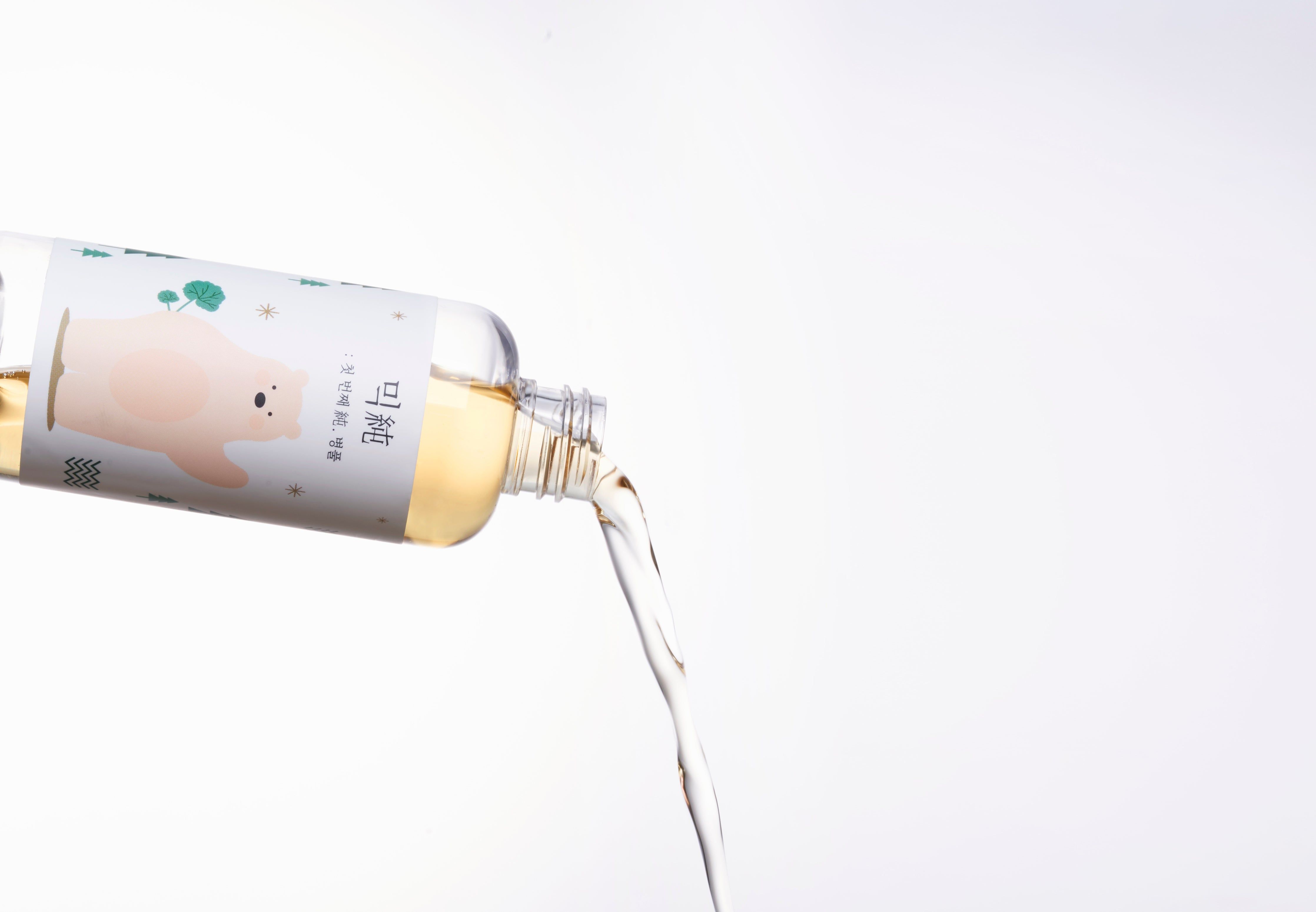 Flüssigkeit fließt aus einer Flasche. Etikett mit Bär-Illustration und Schriftzeichen.