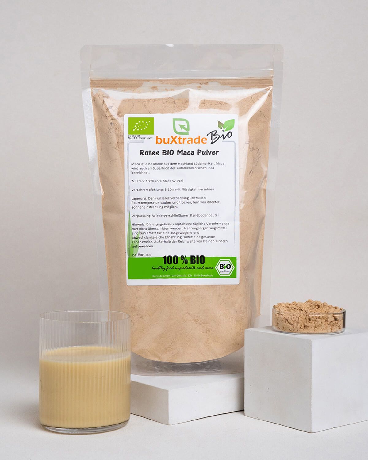 Bio Maca Pulver im Beutel, daneben ein Glas mit Maca-Getränk und eine kleine Schale Pulver.