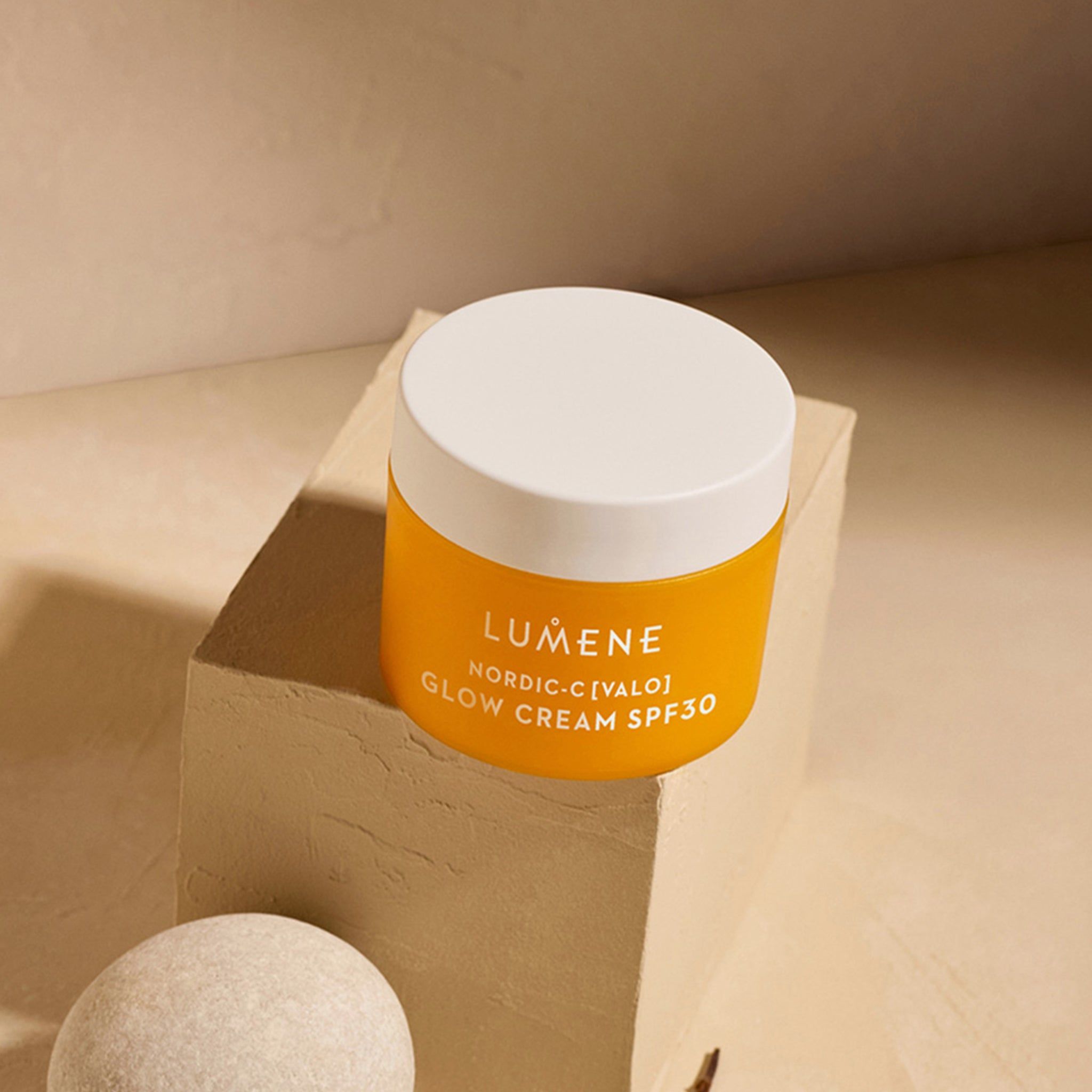 Gelbe Creme-Dose mit weißem Deckel auf einem Sockel. Aufschrift: LUMENE, NORDIC-C [VALO] GLOW CREAM SPF30.