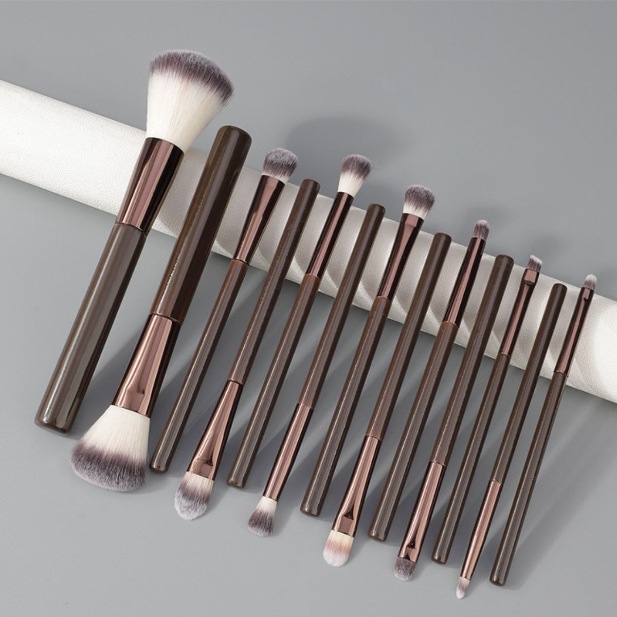 Ein Set aus 12 dunklen Make-up-Pinsel mit roségoldenen Akzenten und weichen Borsten.