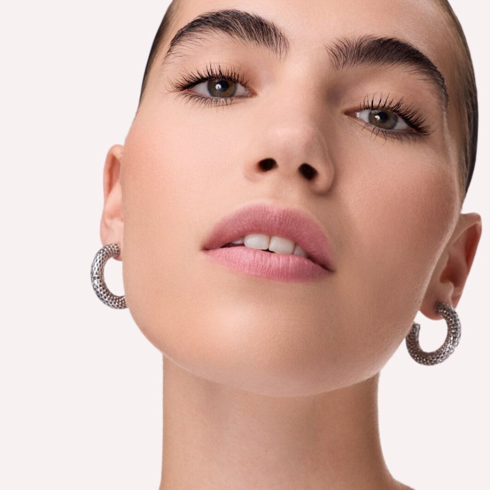 Nahaufnahme eines Gesichts mit silbernen Creolen. Die Frau hat dunkle Augenbrauen und Lippen.