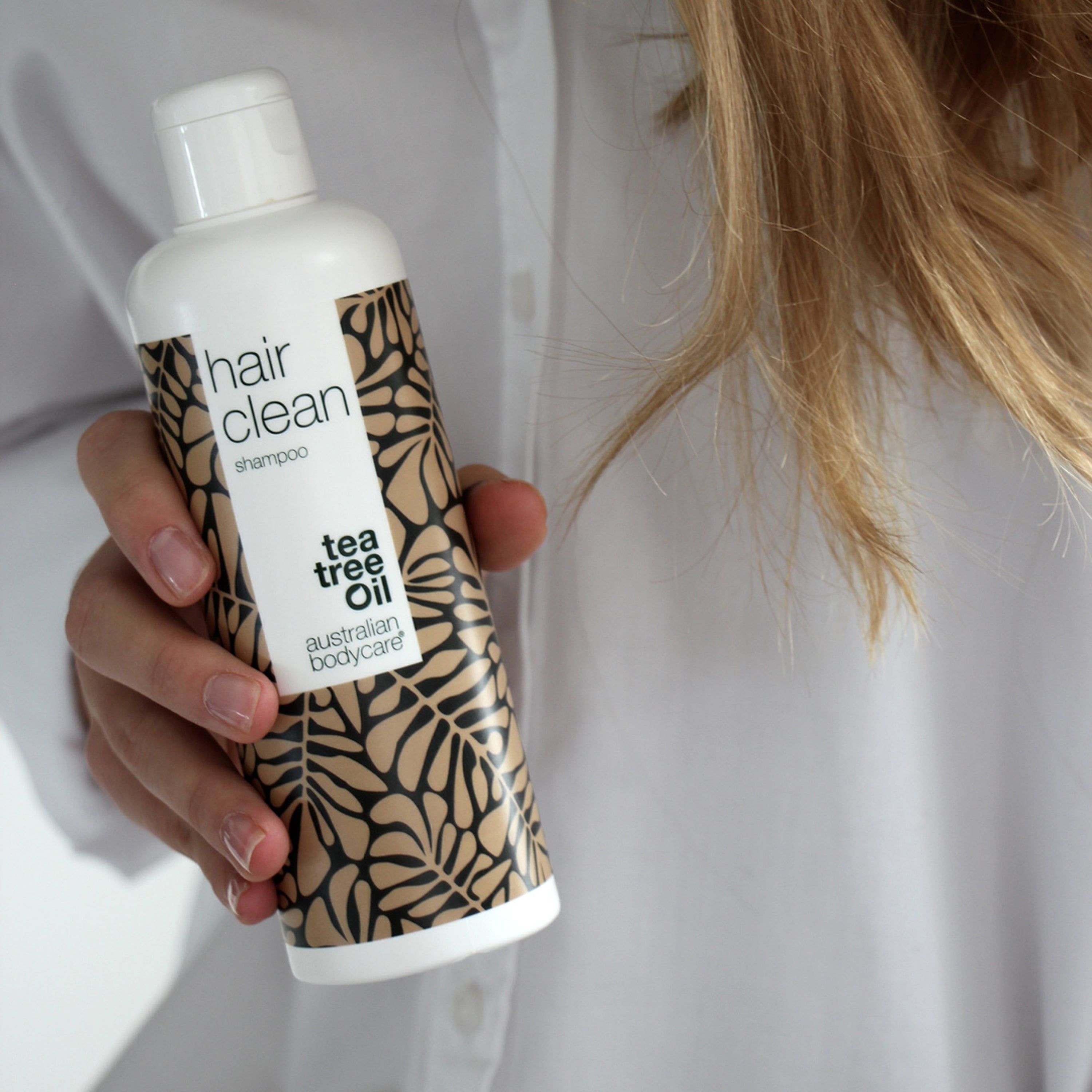 Person hält Flasche Shampoo. Text: hair clean shampoo, tea tree oil, Australian Bodycare.