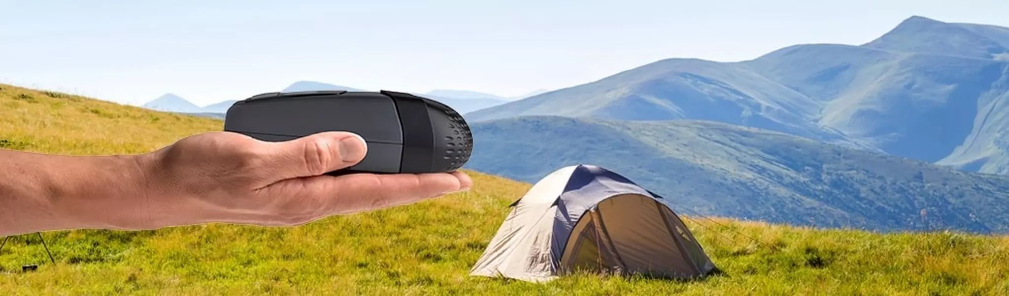 Kompaktes, graues Reise-CPAP-Gerät in einer Hand, vor Berglandschaft und Zelt.