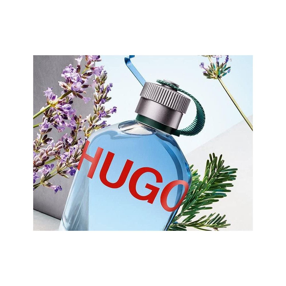Hellblaues Hugo Boss Parfümflakon mit rotem HUGO-Schriftzug. Silberner Verschluss, grüne Schlaufe. Lavendel und Grünzweige.