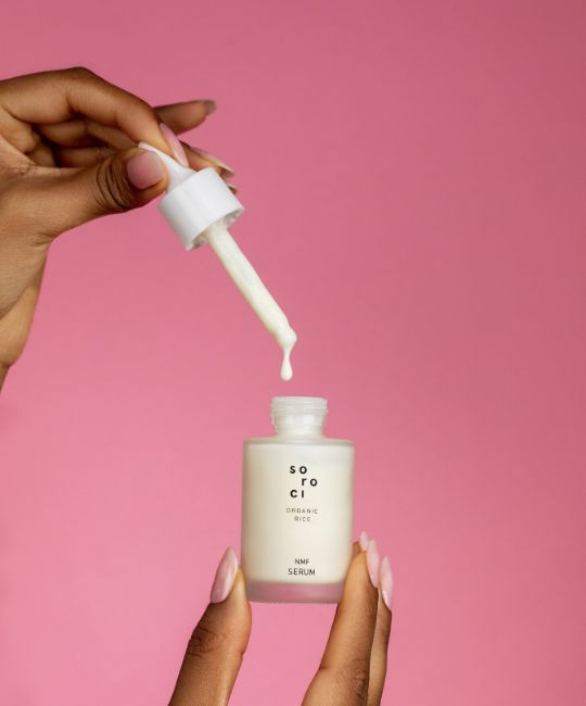 Serumflasche mit Pipette. Weißer Deckel, Aufschrift. Tropfen Serum. Rosa Hintergrund.