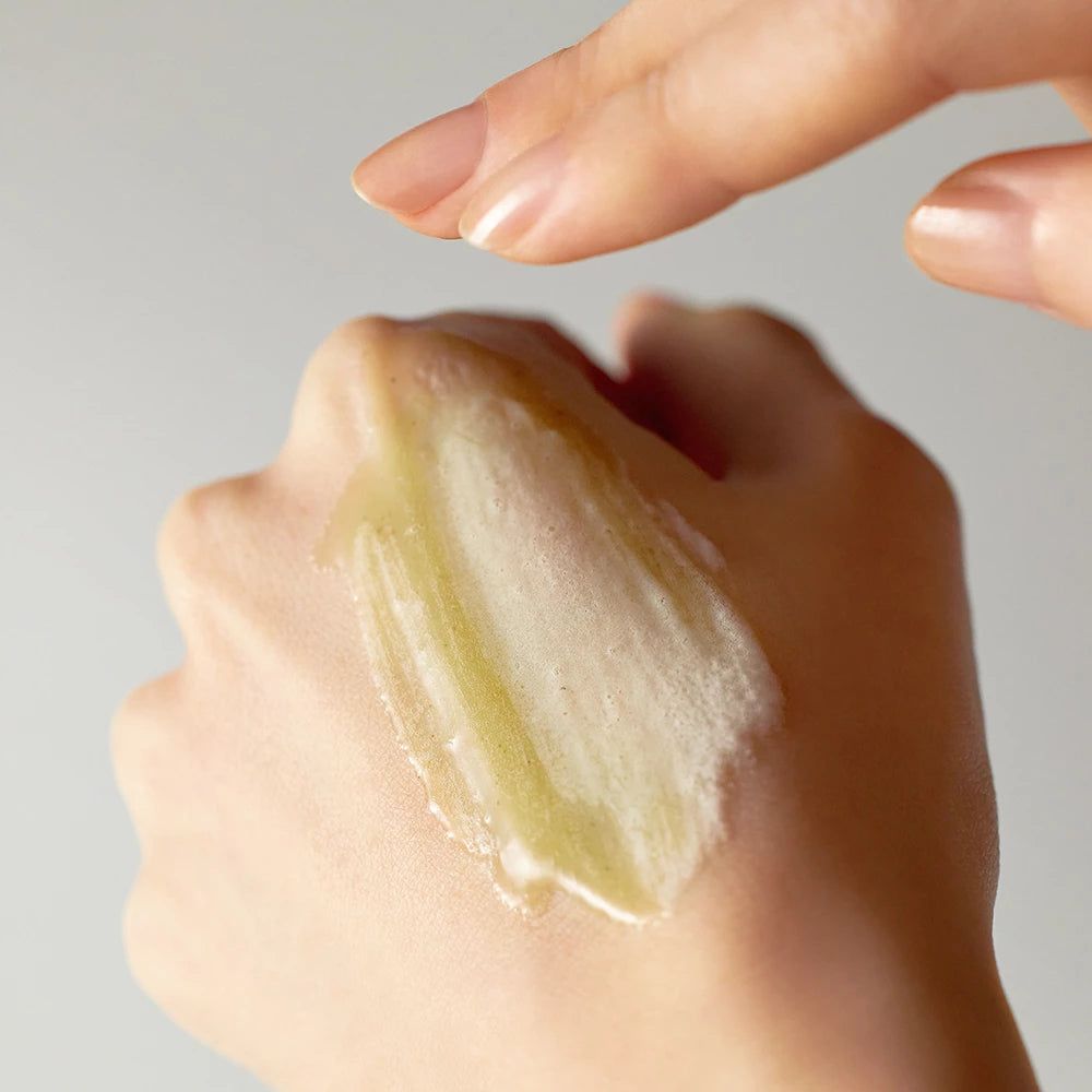 Hand mit gelartiger Substanz. Eine andere Hand berührt die Substanz. Keine Produktbezeichnung sichtbar.