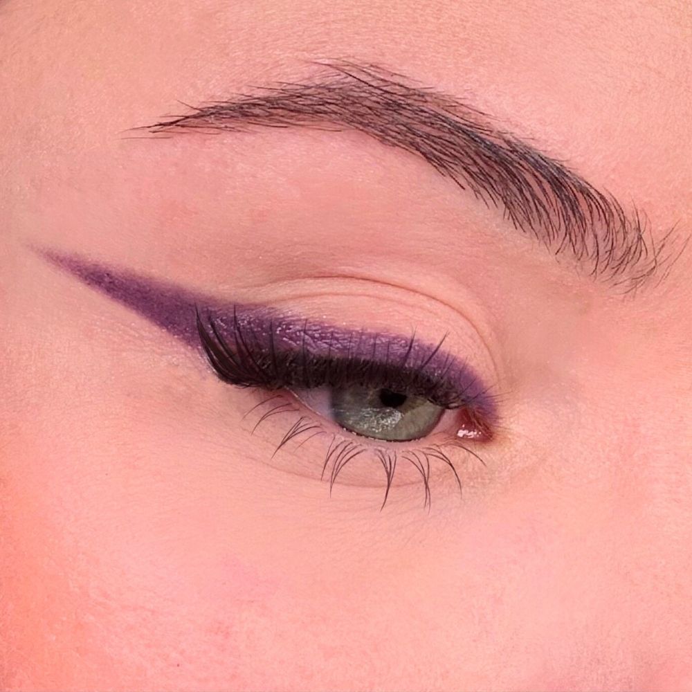 Auge mit violettem Eyeliner. Augenlid mit violettem Eyeliner. Braue und Wimpern sichtbar.