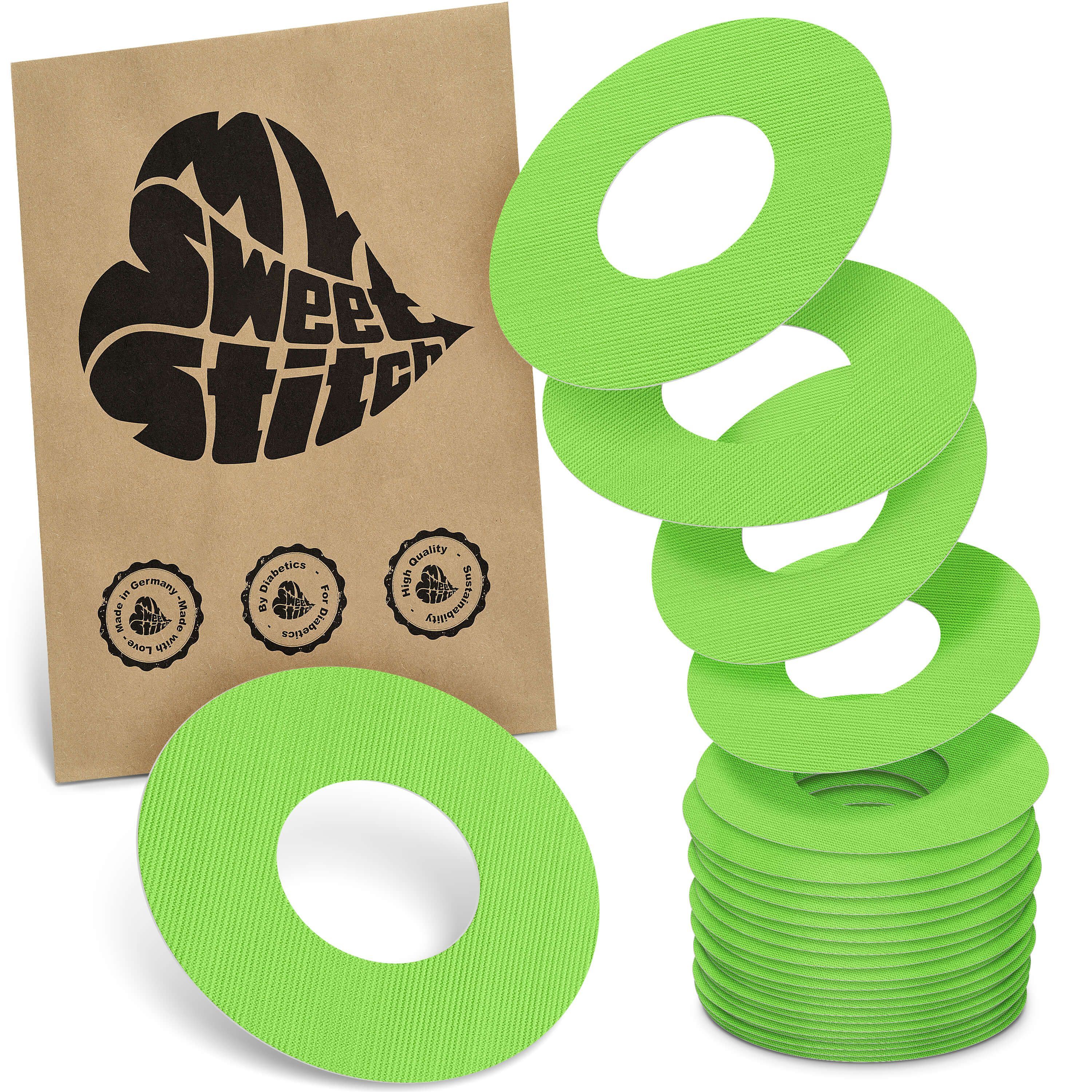 Grüne, runde Fixierringe mit Loch. Verpackung mit Logo und Qualitätssiegeln. Stapel und einzelne Ringe sichtbar.