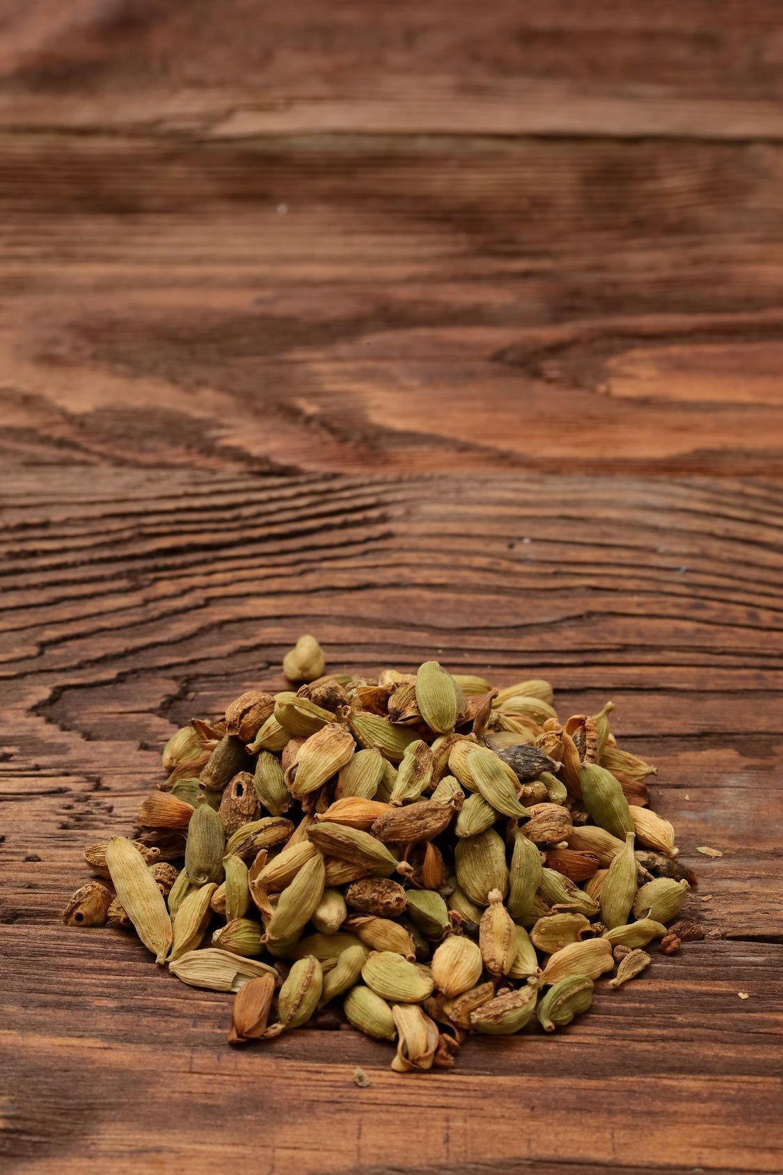 Haufen Kardamomkapseln auf Holz. Grüne und beige Kapseln. Holzmaserung im Hintergrund.