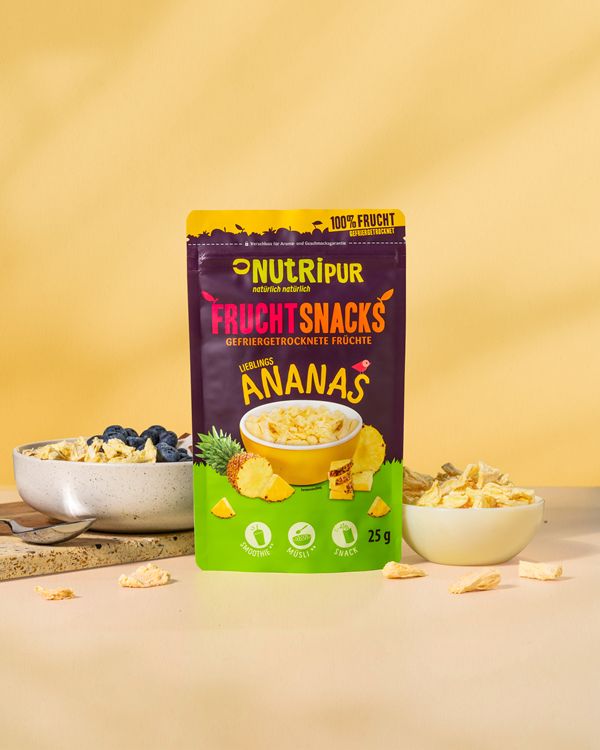 Gefriergetrocknete Ananas-Bits in Schalen und Verpackung. Aufschrift: "NutriPur Fruchtsnacks Ananas". 25g.