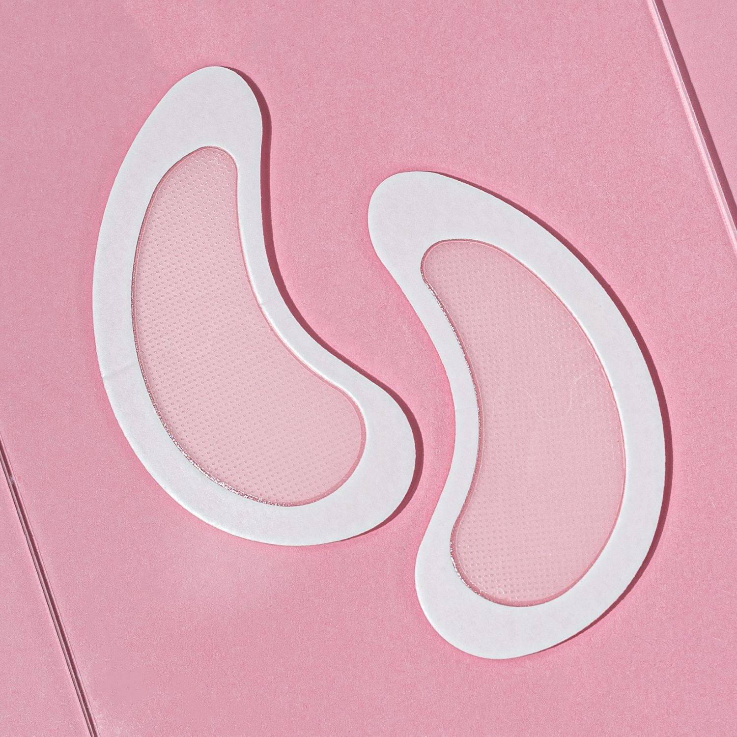 Zwei weiße, augenförmige Pads mit einem hellen Netz. Auf rosa Hintergrund.