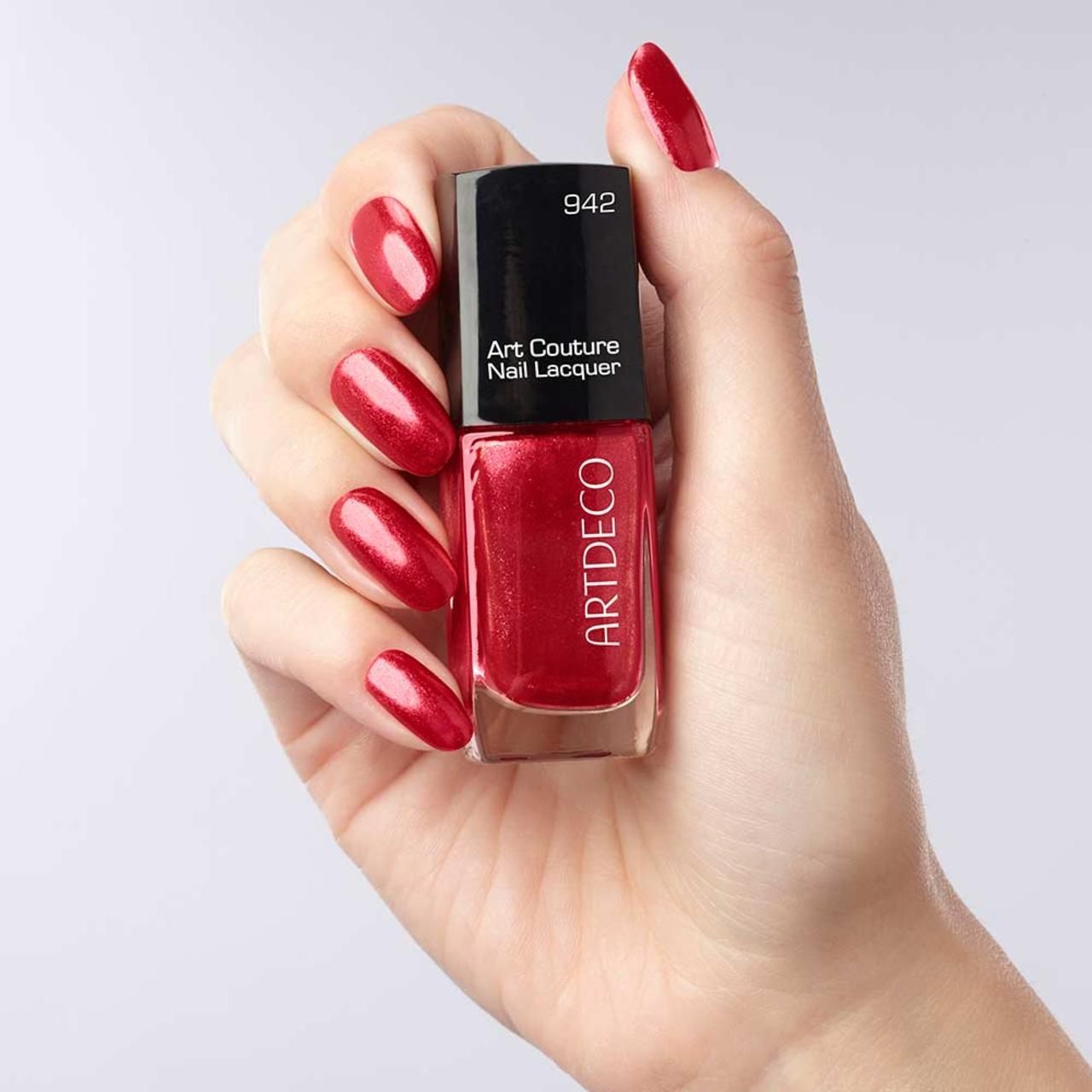 Hand hält Nagellackflasche und lackierte Nägel. Roter Nagellack, Aufschrift: Art Couture Nail Lacquer, ARTDECO, 942.