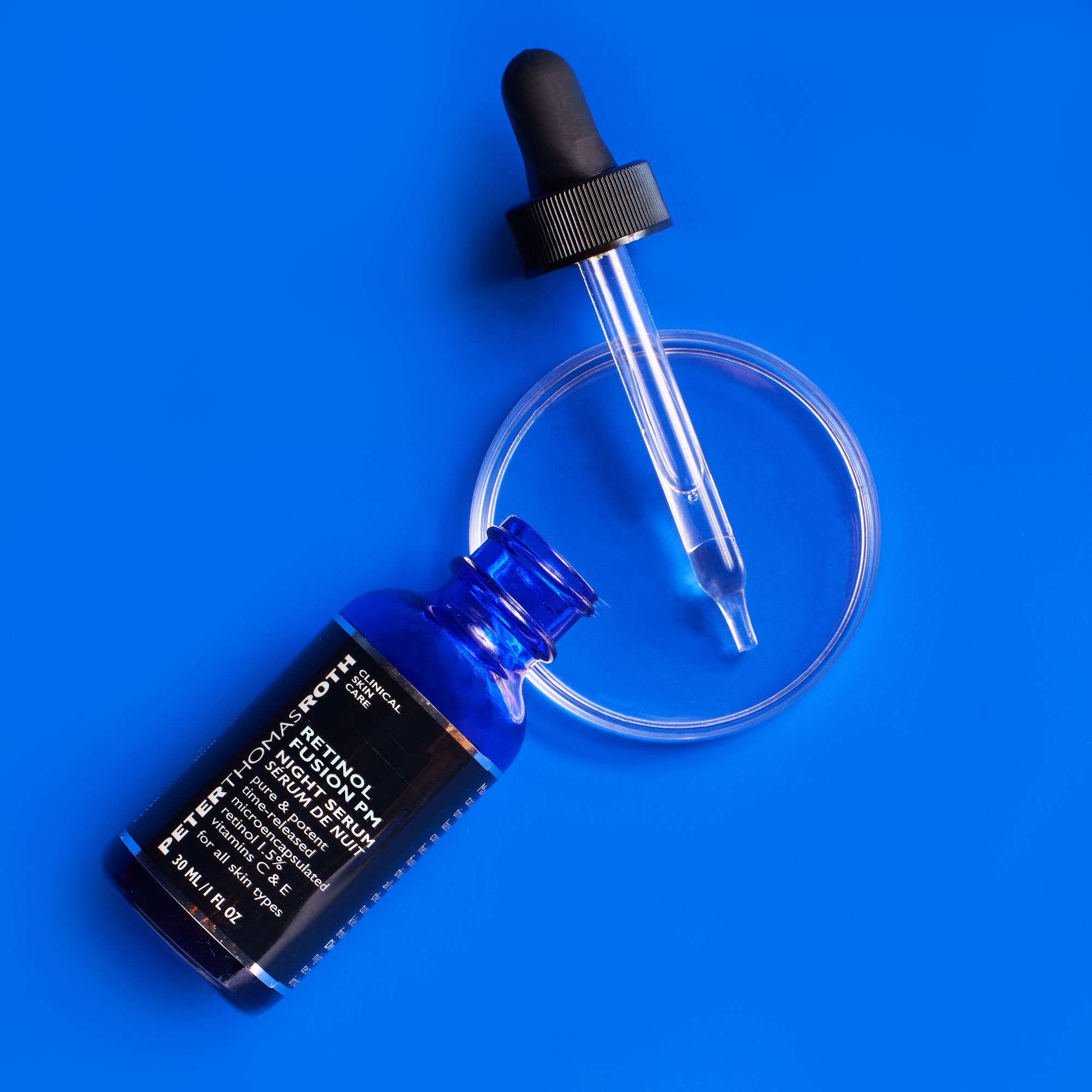 Blaue Glasflasche mit schwarzem Deckel und Pipette, daneben eine leere Petrischale. Blaues Hintergrund.