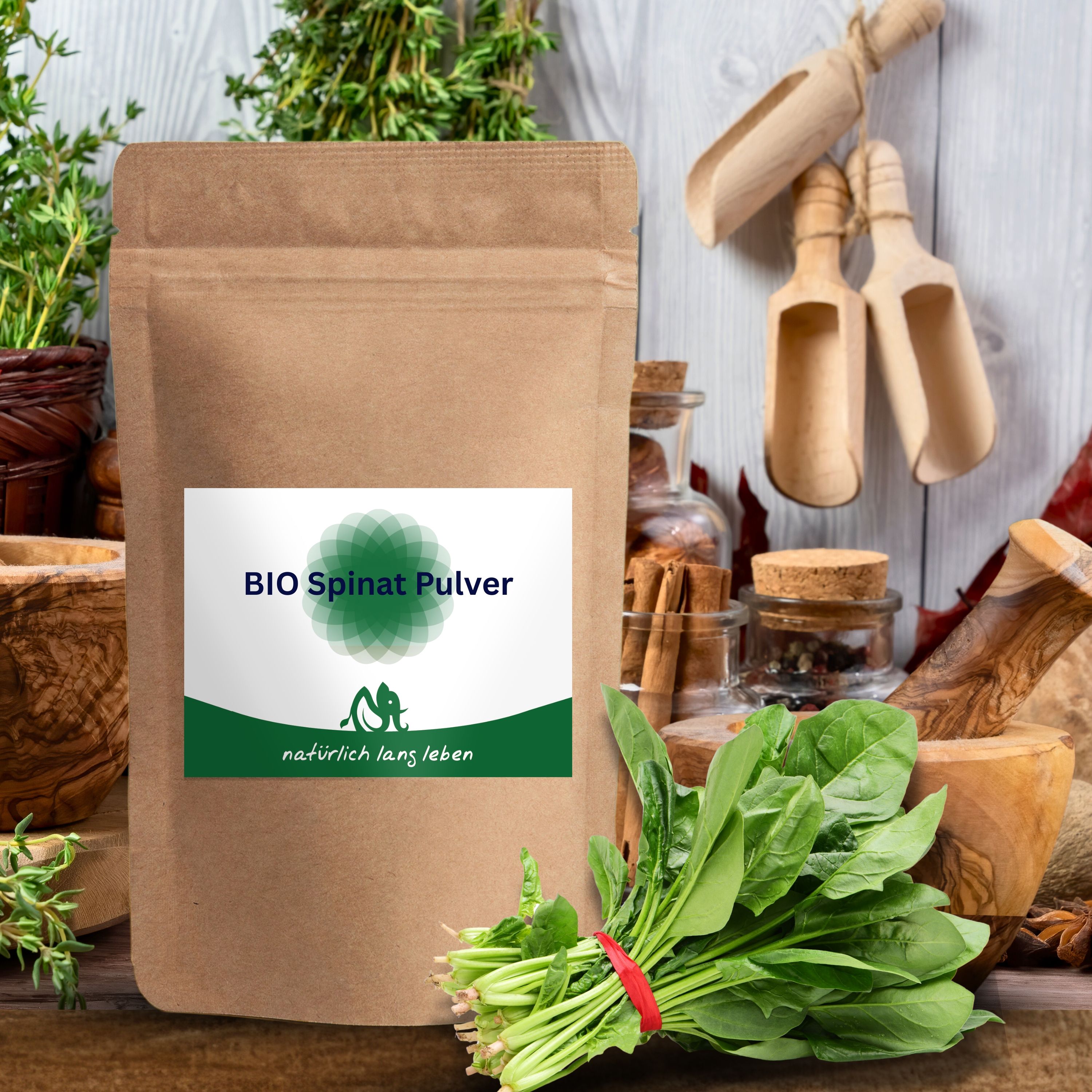 BIO Spinat Pulver Beutel, umgeben von frischem Spinat, Kräutern und Küchenutensilien. Aufschrift: BIO Spinat Pulver und natürlich lang leben.