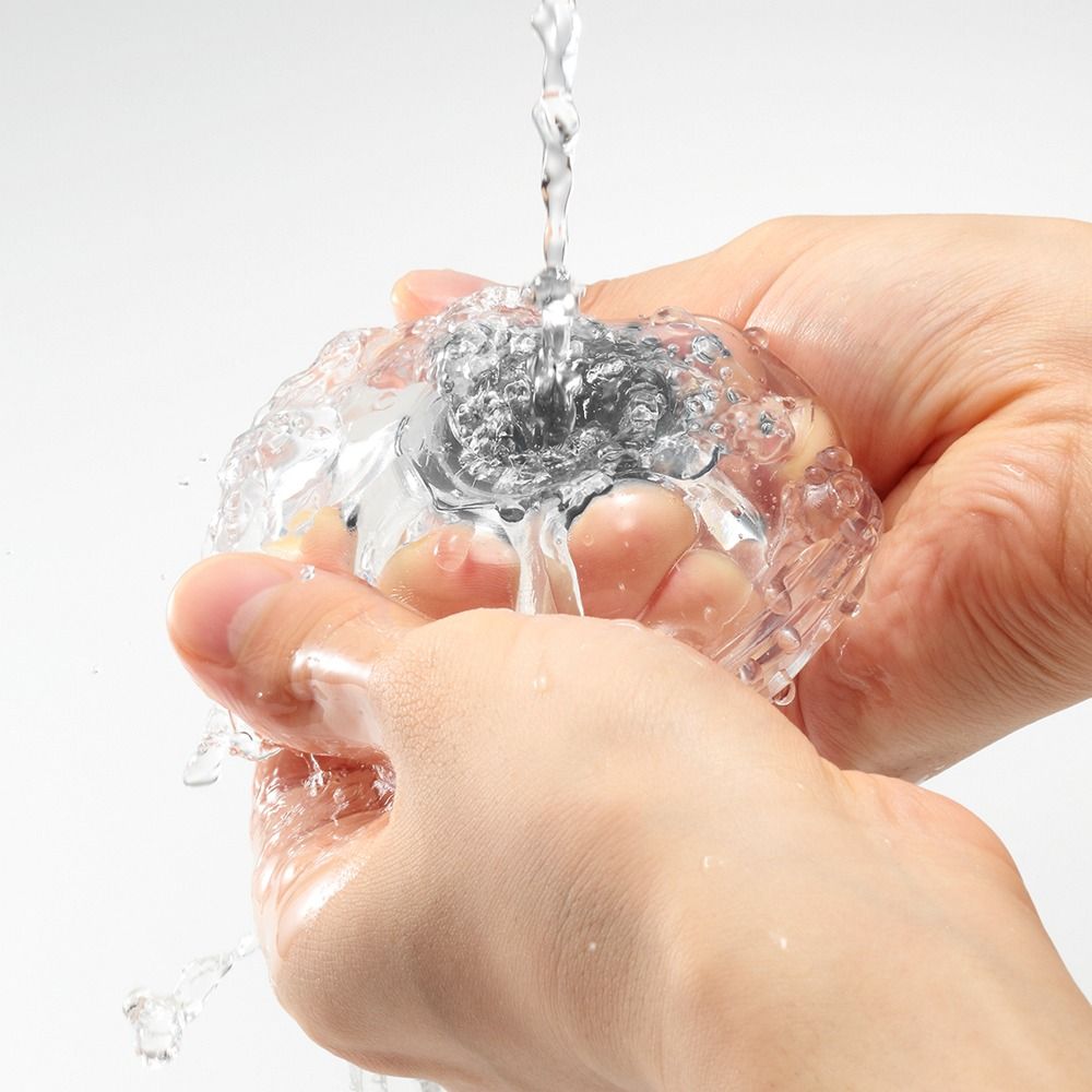 Hände waschen ein transparentes Masturbationsgerät unter fließendem Wasser. Wasser ist sichtbar.