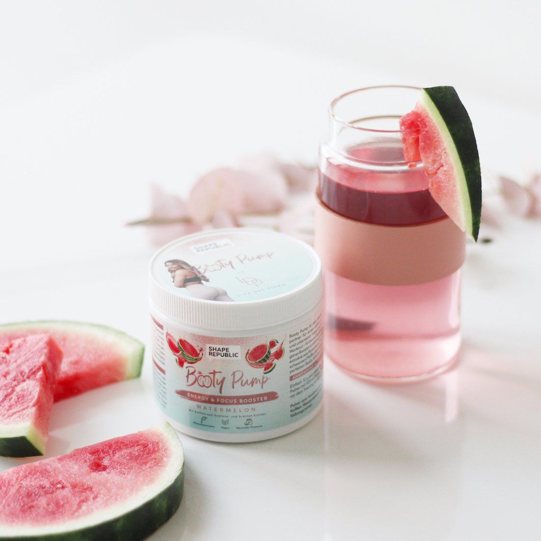 Produktglas mit "Booty Pump" neben Glas mit rosa Getränk und Wassermelone. Rosa Blütenblätter.