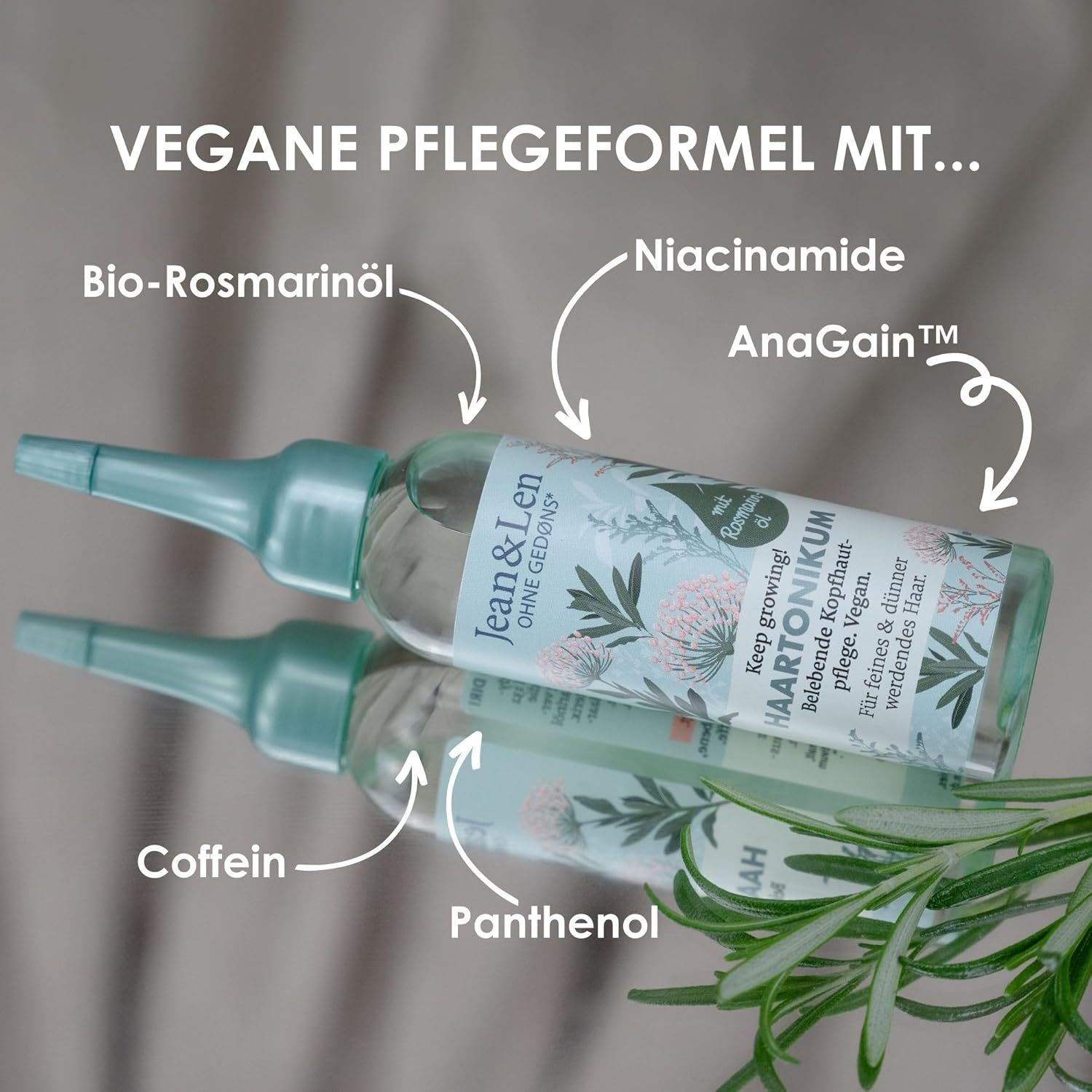 Haartonikum-Flasche mit Spiegelung. Beschriftung: Bio-Rosmarinöl, Niacinamid, AnaGain, Coffein, Panthenol. Logo: Jean & Len OHNE GEDØNS*.
