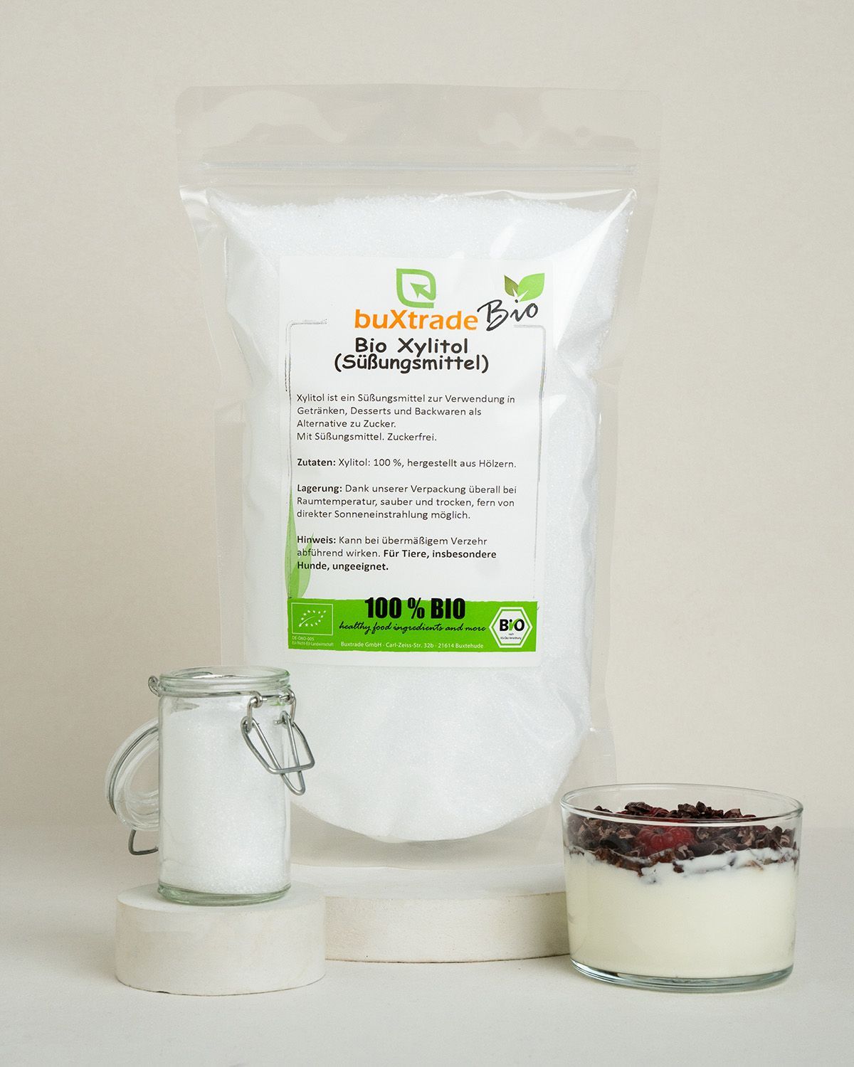 Ein Beutel buXtrade Bio Xylit (Süßungsmittel) neben einem Glas Xylit und einem Dessert.