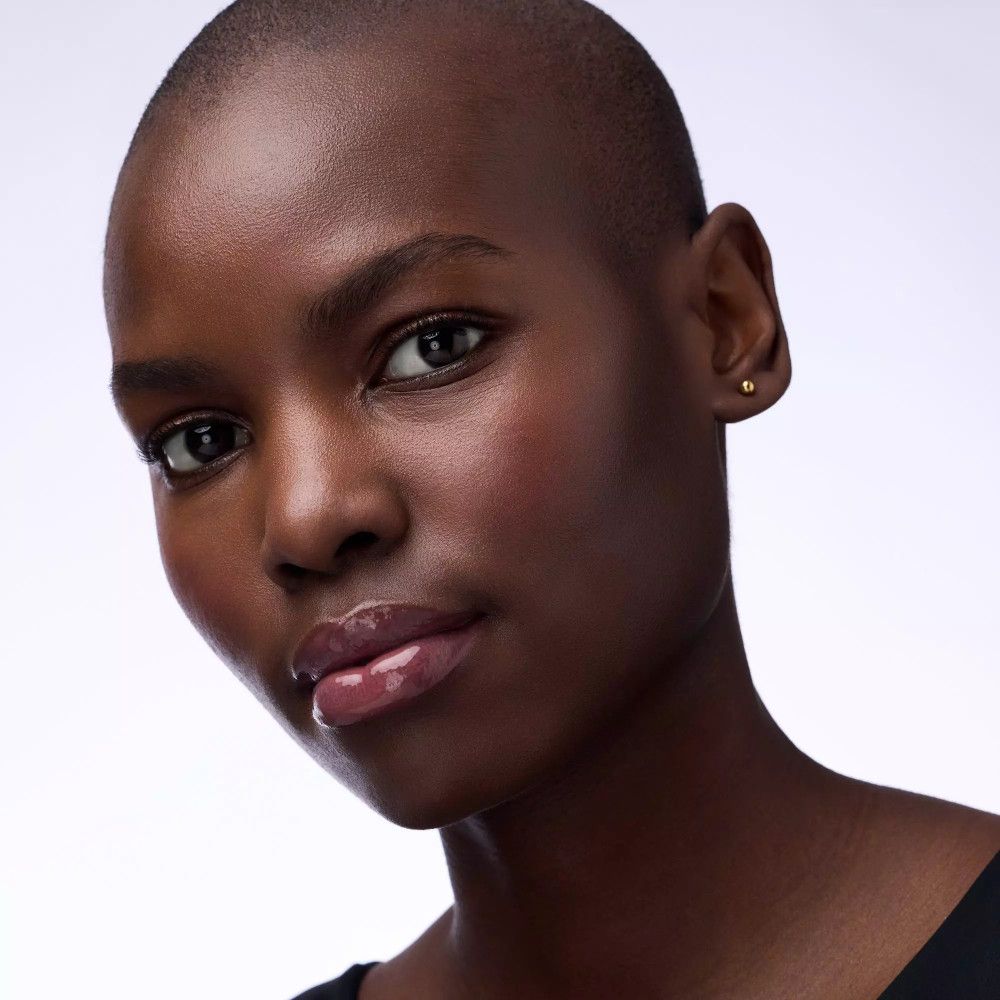 Nahaufnahme einer Frau mit rasierten Haaren. Sie hat glänzende Lippen. Hautton ist dunkel.