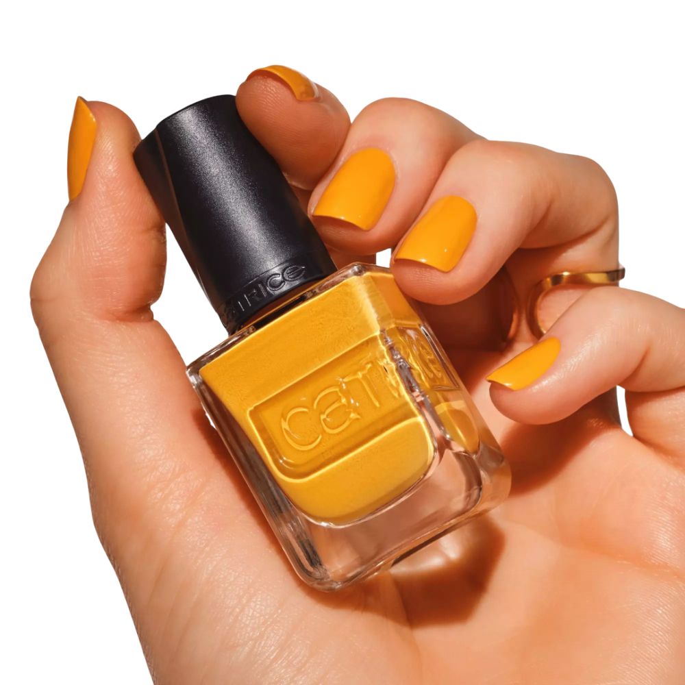 Hand hält Nagellack-Flasche. Gelber Nagellack auf Nägeln und Flasche. Marke Catrice sichtbar. Quadratische Flasche.