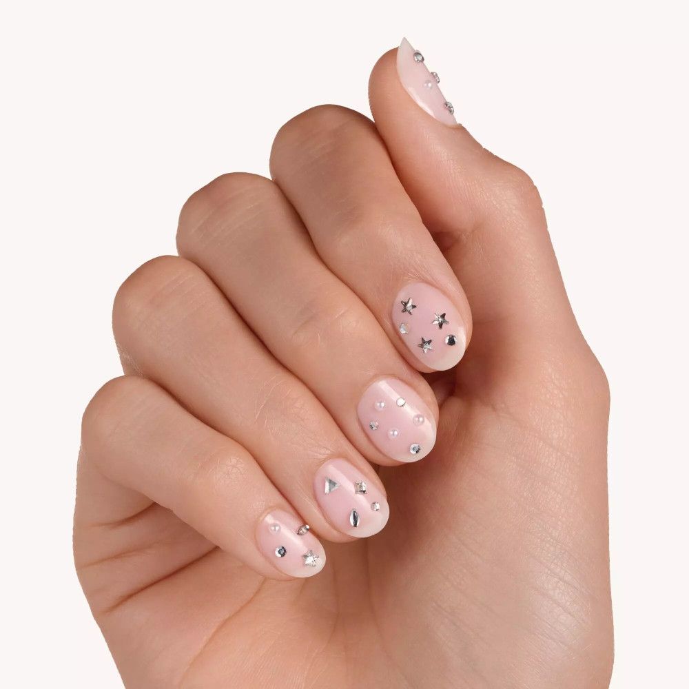 Hand mit lackierten Nägeln, verziert mit silbernen Nagelstickern in Stern-, Tropfen- und Quadratformen.