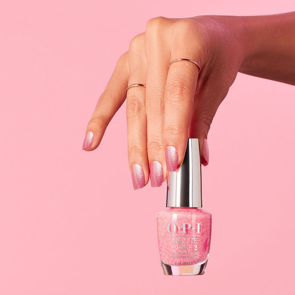 Hand hält eine Flasche Nagellack. Rosa Nagellack mit Glitzer. OPI Infinite Shine.