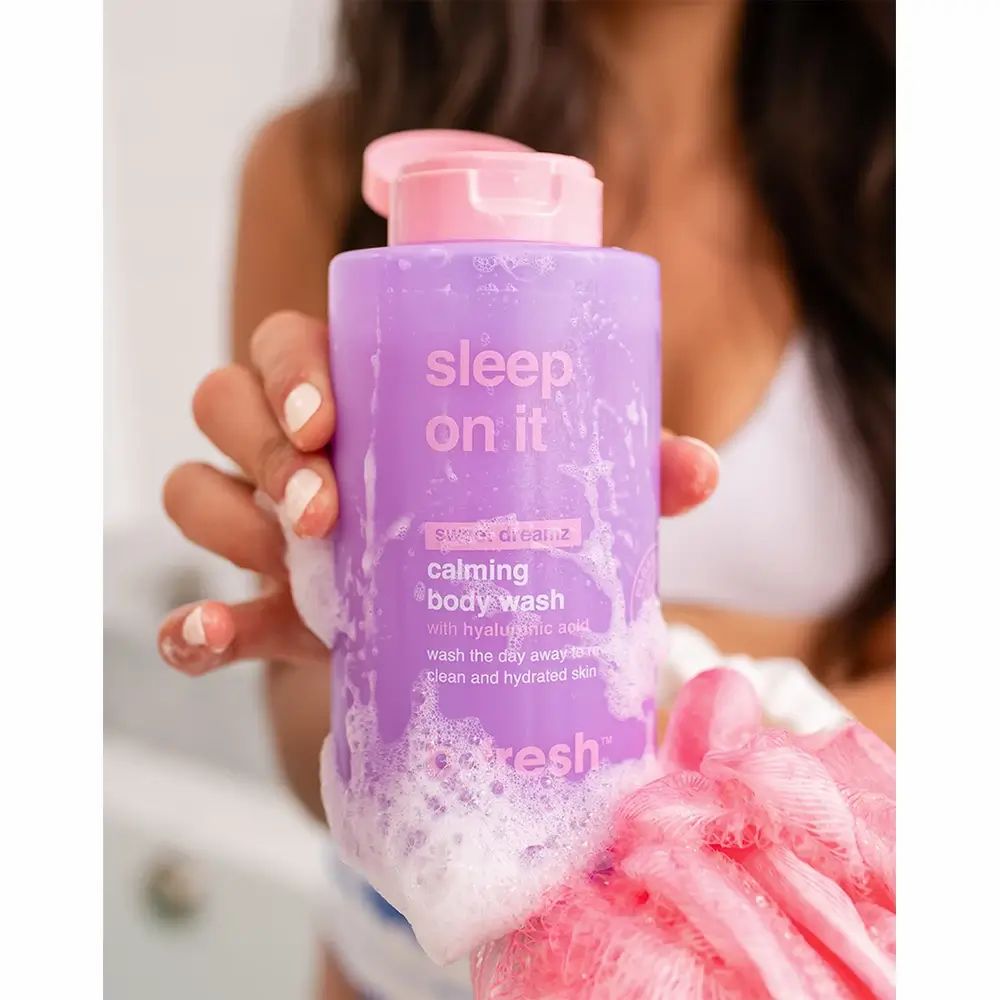 Lila Duschgel-Flasche mit rosa Deckel. Text: "sleep on it", "calming body wash". Produkt wird von einer Person gehalten, Schaum umhüllt die Flasche.
