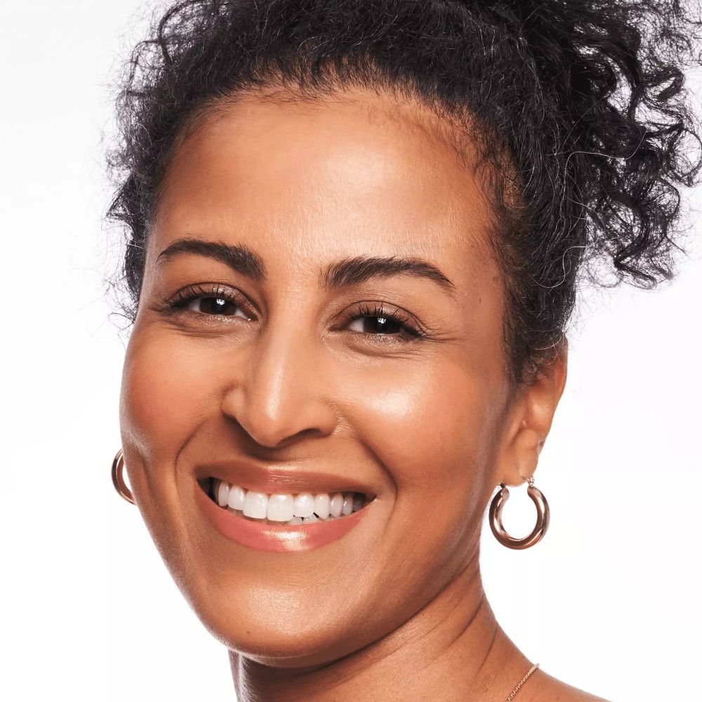 Porträt einer Frau mit gebräunter Haut, die lächelt. Sie trägt goldene Creolen.